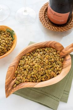 a wooden bowl filled with green seeds next to a bottle of wine and napkins