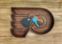 a wooden key holder with two keys in it on top of a wood table next to a pair of scissors