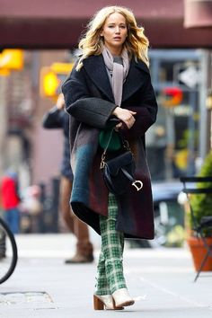 the blonde woman is walking down the street wearing plaid pants and a black coat with an overcoat