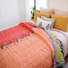 a bed with an orange comforter and pillows on top of it, next to a potted plant