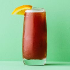 a tall glass filled with red liquid and an orange slice on the rim, sitting on a green surface