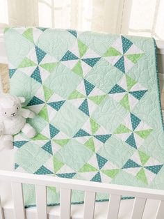 a baby crib with a green and white quilt on top of it, next to a teddy bear