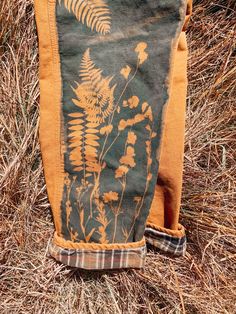 an old pair of jeans sitting in the middle of some dry grass, with a fern print on it