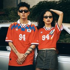 two people standing next to each other in front of a car wearing matching shirts and sunglasses