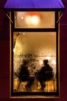 two people sitting at a table in front of a window with an umbrella over it