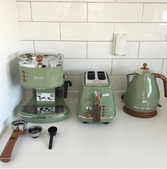 two green coffee makers sitting on top of a counter next to each other in front of a white tiled wall