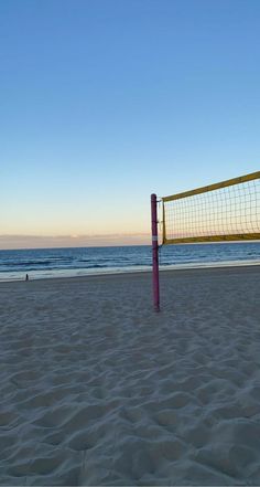 a volleyball net on the beach with people playing in the water behind it at sunset