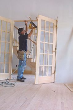 a man is using a power drill on the wall in an unfinished room with wood floors