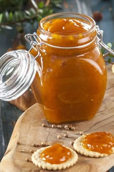 a jar filled with jam sitting on top of a wooden cutting board next to crackers