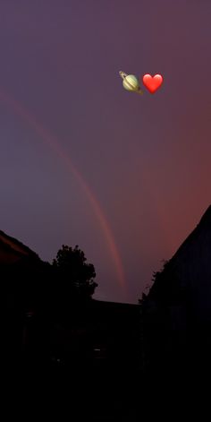 two heart shaped balloons flying in the sky at night with a rainbow behind them and a house