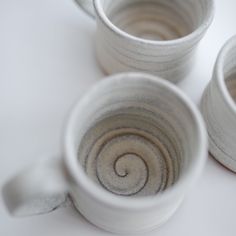 three white cups sitting on top of a table next to each other with swirl designs in them