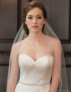 a woman in a wedding dress wearing a veil with beading on the side and shoulder