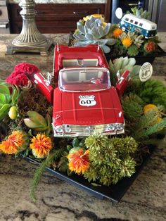 a red toy car sitting on top of a table filled with flowers and succulents