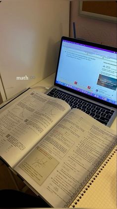 an open book sitting on top of a laptop computer next to a notebook and pen