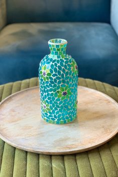 a blue and green vase sitting on top of a wooden tray next to a couch