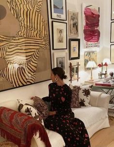 a woman sitting on top of a couch in front of a wall covered with pictures