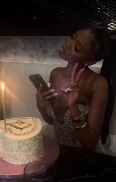 a woman holding a cell phone in front of a cake with a candle on it