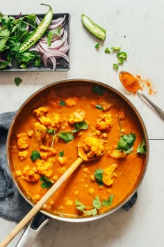 a pan filled with cauliflower and red curry next to a bowl of cilantro