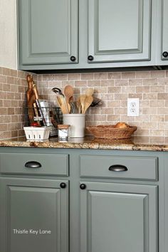 a kitchen with gray cabinets and wooden utensils on the counter top in front of a brick backsplash