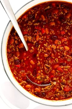 a white bowl filled with chili and beans on top of a table next to a spoon