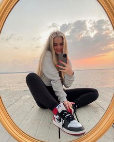 a woman sitting on the ground taking a selfie with her phone in front of an oval mirror