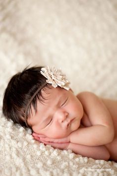 a baby sleeping on top of a white blanket wearing a flower in its hair and headband