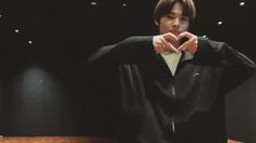 a young man in a black shirt is making a heart sign with his hands while sitting at a table