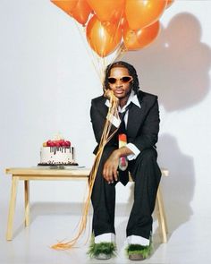 a man sitting in front of a cake and balloons