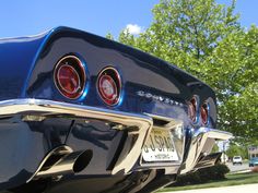 the rear end of a classic car parked in front of a tree on a sunny day