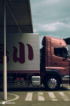 a red semi truck parked in front of a large metal structure with the word u on it's side