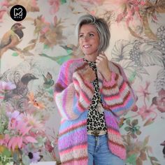 a woman standing in front of a wall with flowers on it wearing a colorful sweater