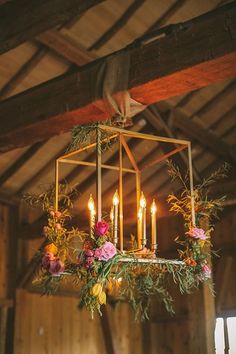 a chandelier with flowers and candles hanging from it's ceiling in a barn