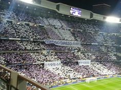 a stadium filled with lots of people sitting on top of a soccer field at night