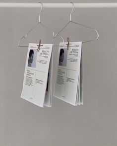 two papers hanging from clothes pins on a metal rod with clips attached to them, in front of a gray wall