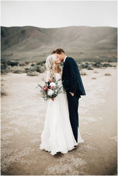 a bride and groom kissing in the desert