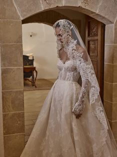 a woman in a wedding dress is standing near an archway with a veil on her head