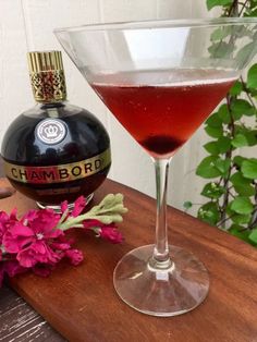 a bottle of champagne next to a glass filled with liquid and flowers on a wooden table