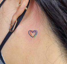 a woman's behind the ear tattoo with a rainbow heart on her left side