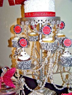 a cake and cupcakes are displayed on a silver stand with red ribbon around it