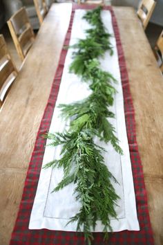 a long table is decorated with evergreen branches and red checkered runner on the top