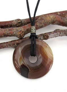 Brown Stripe Agate Natural Semi-Precious Gemstone Donut Energy Pendant Necklace 40mm.  ED334-B / ED334-E / ED334-F. Measures approx. 40 x 8mm = 1 ½" x ¼".   Suspended on a continuous 31" satin finish black cord strand without a clasp closure and accented with a bronze tone Tibetan style bead. Makes a unique gift for any occasion.  The one you choose is the one you will receive.  From a smoke and pet free environment.   You can always check the internet for the meaning, physical and healing prope Cheap Rustic Brown Jewelry, Unique Brown Jewelry At Cheap Price, Luxury Brown Nature-inspired Necklaces, Luxury Brown Earthy Jewelry, Luxury Earthy Brown Jewelry, Luxury Brown Agate Necklace, Luxury Brown Natural Stones Jewelry, Cheap Brown Circular Jewelry, Luxury Brown Necklace With Large Pendant