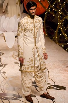 a man in a white sherwa with gold embroidery on the jacket and pants