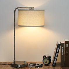 a lamp that is on top of a table next to some books and an alarm clock