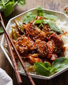 a white bowl filled with meat and vegetables on top of rice next to chopsticks