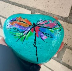 a hand holding a painted rock with a dragonfly on it