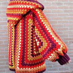 a colorful crocheted blanket draped on top of a pole next to a brick wall