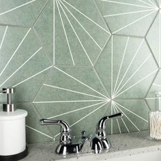 two chrome faucets sitting next to each other on a counter top in front of a tiled wall