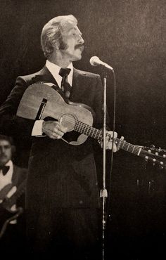 a man in a suit and tie holding a guitar while standing next to a microphone