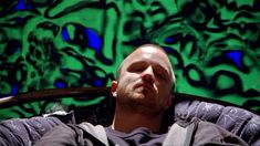 a man sitting in front of a green wall with black and white graffiti on it