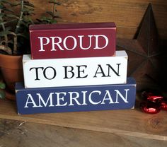 three wooden blocks with the words proud to be an american on them sitting next to a potted plant